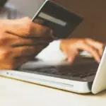a man holding a credit card while using a laptop